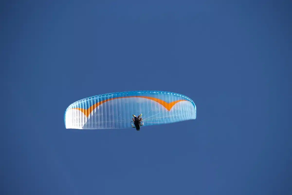 Esquiador en descenso con parapente pequeño, fusionando esquí y vuelo