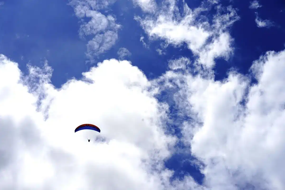 Deportista en vuelo sobre nieve alpina con equipamiento de parapente, montañas al fondo