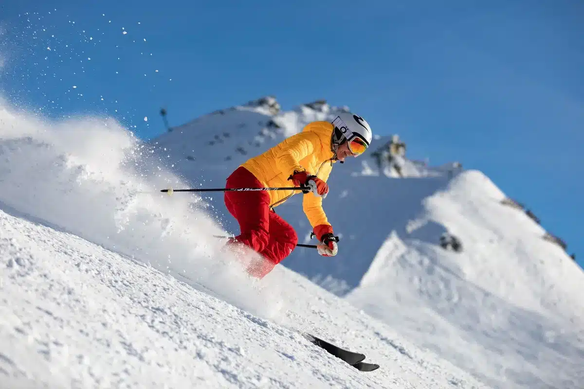 Esquiador solitario bajando por un corredor alpino empinado rodeado de picos nevados